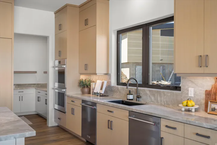 Kitchen featuring light wood finish cabinets, light stone counters, stainless steel appliances, and dark wood-style flooring