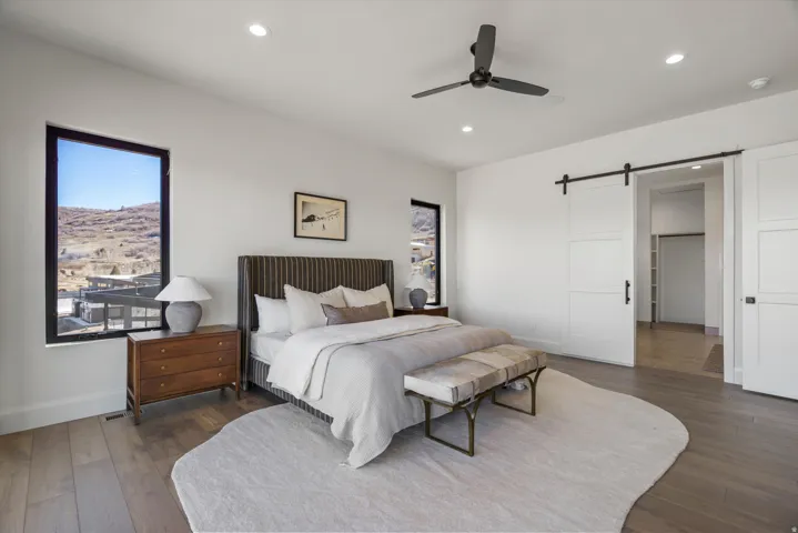 Bedroom featuring a barn door, dark wood-type flooring, a ceiling fan, and recessed lighting