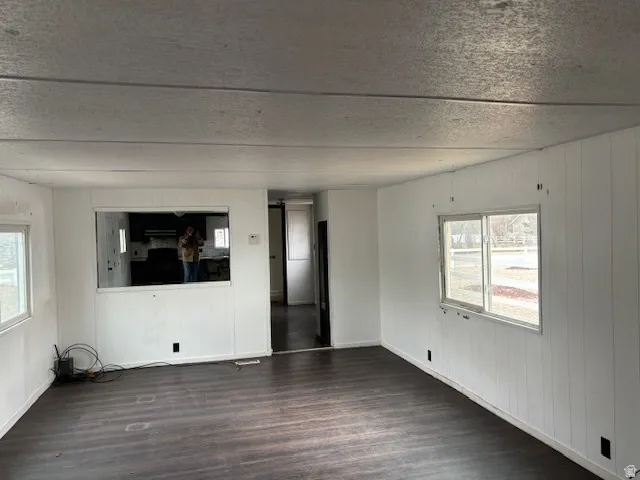 Unfurnished living room with wood walls, dark wood-style floors, and a textured ceiling