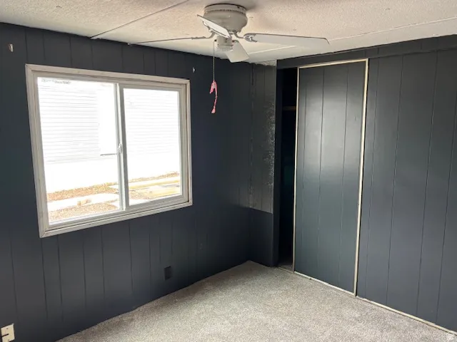 Unfurnished bedroom with wood walls, carpet flooring, ceiling fan, and a textured ceiling