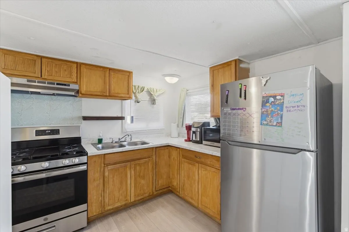 Kitchen featuring stainless steel appliances, light countertops, brown cabinetry, and under cabinet range hood