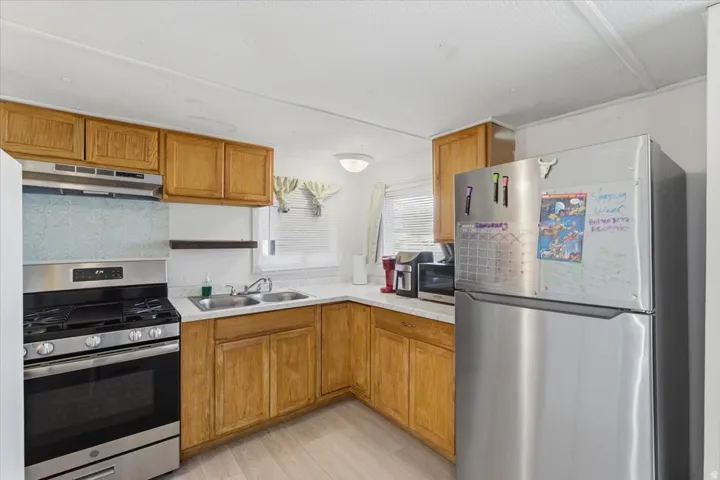Kitchen featuring stainless steel appliances, light countertops, brown cabinetry, and under cabinet range hood