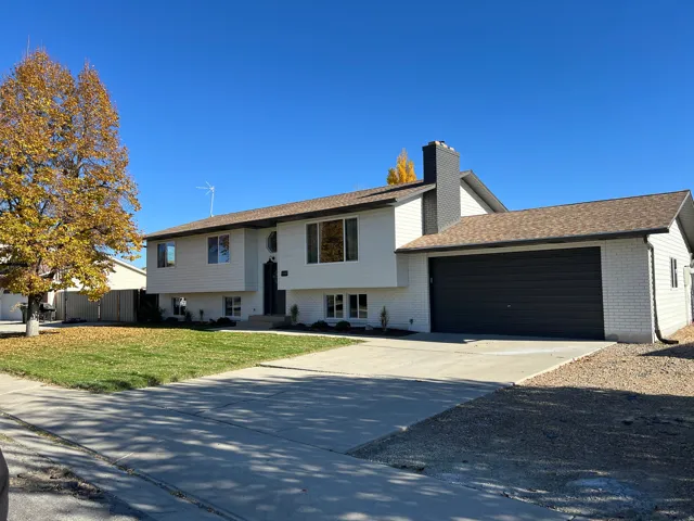 Split foyer home featuring brick siding, driveway, an attached garage, a chimney, and roof with shingles