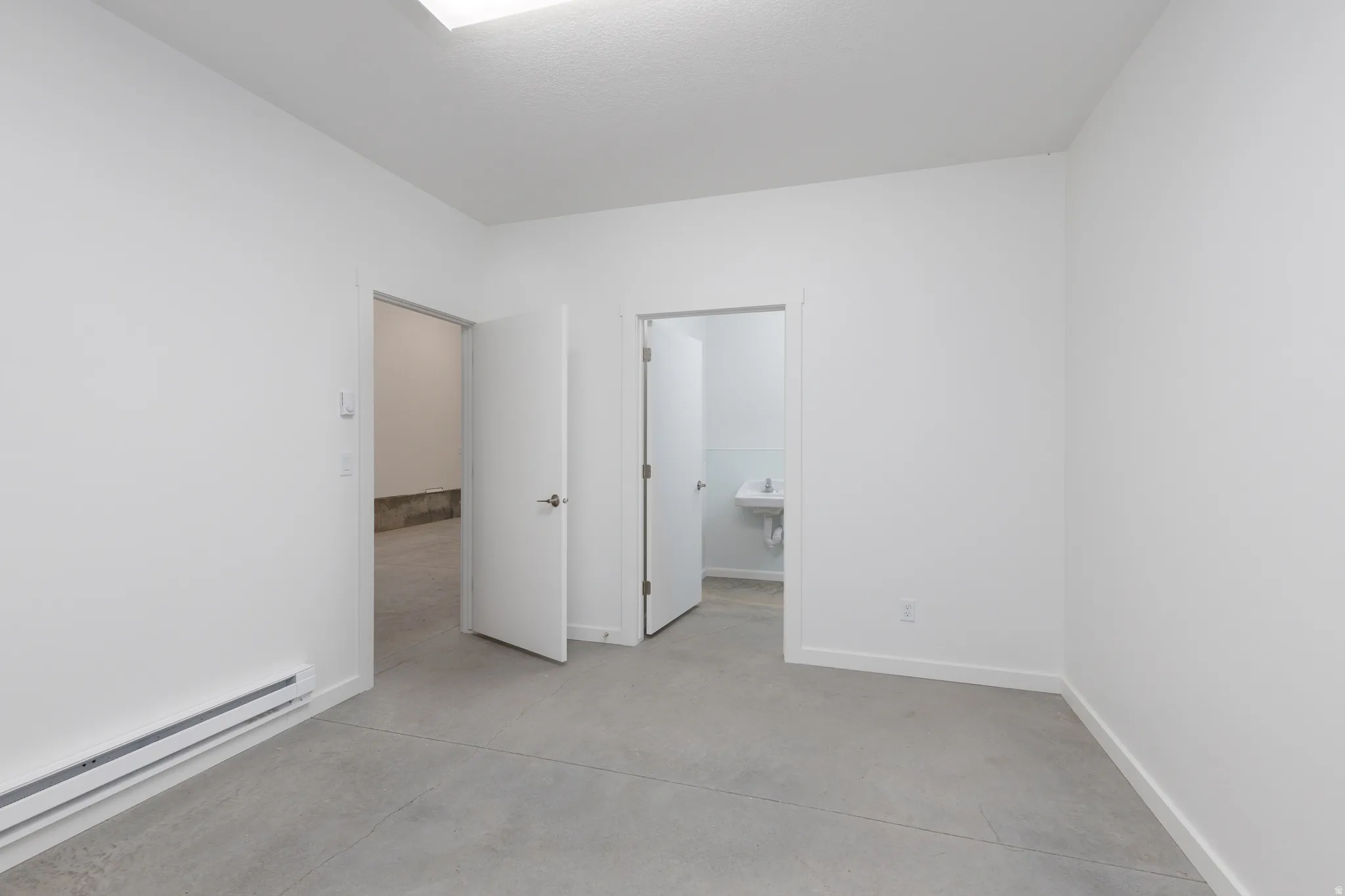 Unfurnished bedroom with baseboard heating, concrete floors, and ensuite bathroom