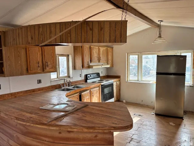 Kitchen with freestanding refrigerator, electric stove, brown cabinets, a peninsula, and pendant lighting