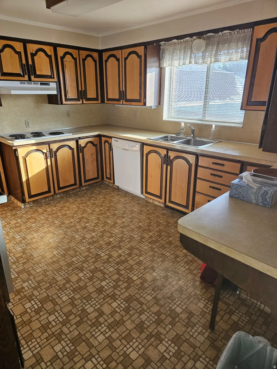 Kitchen with light countertops, white appliances, brown cabinetry, and under cabinet range hood