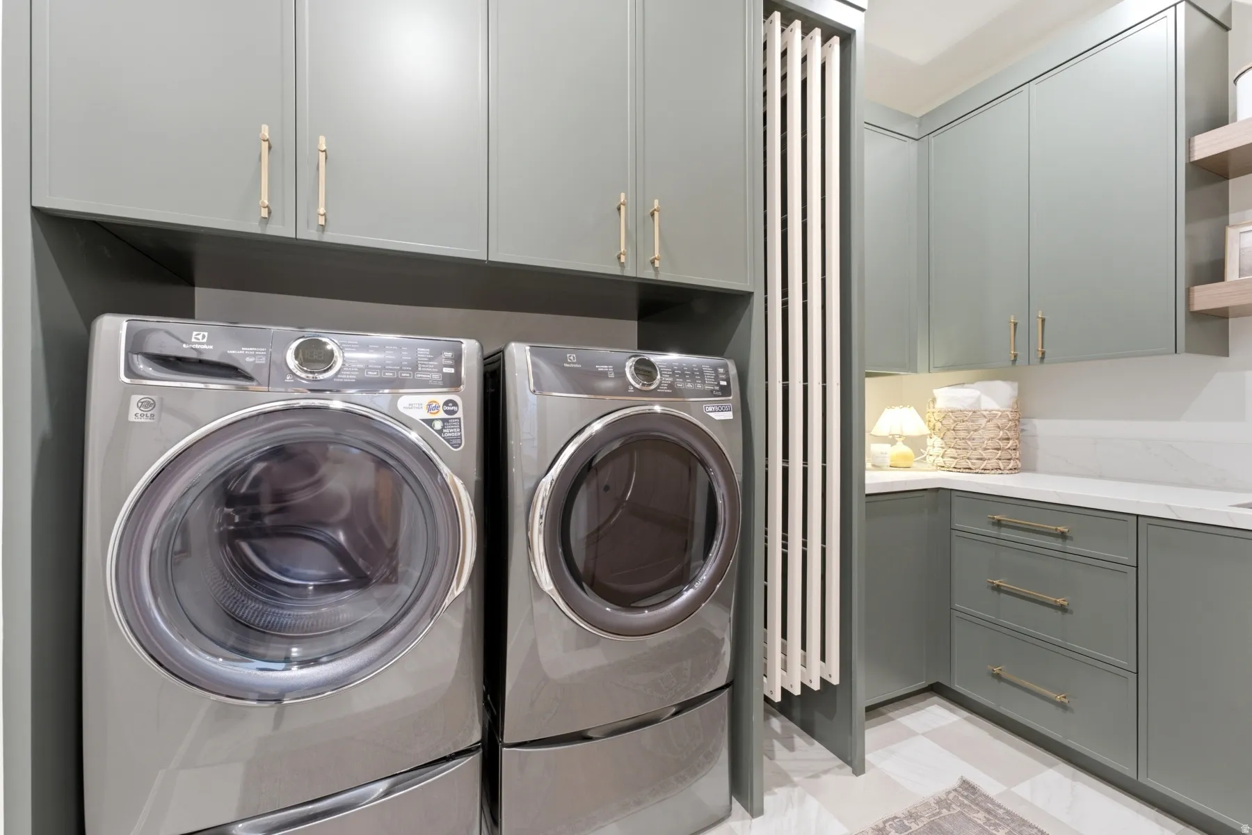 Laundry area featuring sleek grey cabinetry with gold-toned hardware, a built-in folding rack, and a white countertop