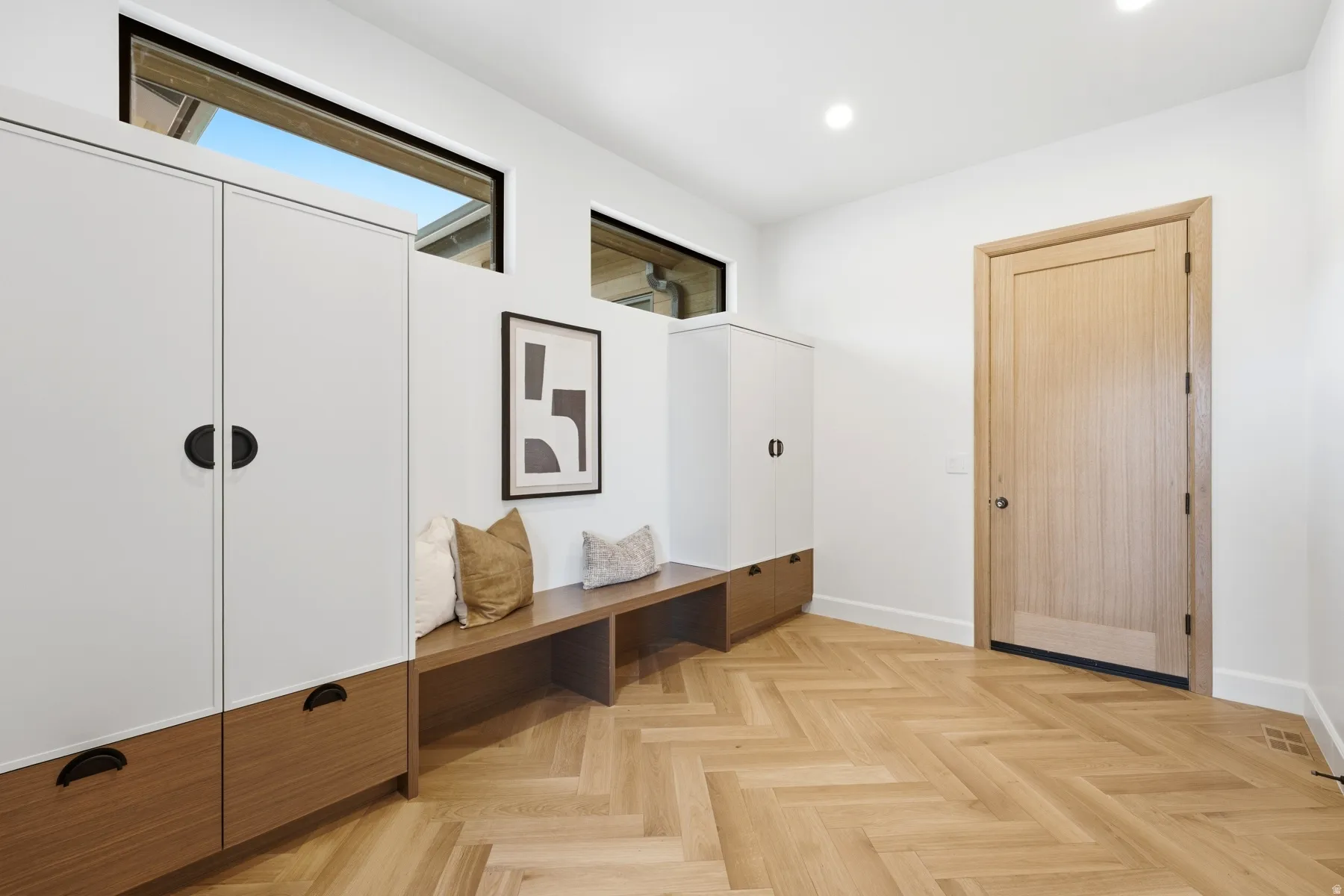 Entryway featuring herringbone wood-finish flooring, integrated white and wood-finish cabinetry, a built-in wood bench, and transom windows
