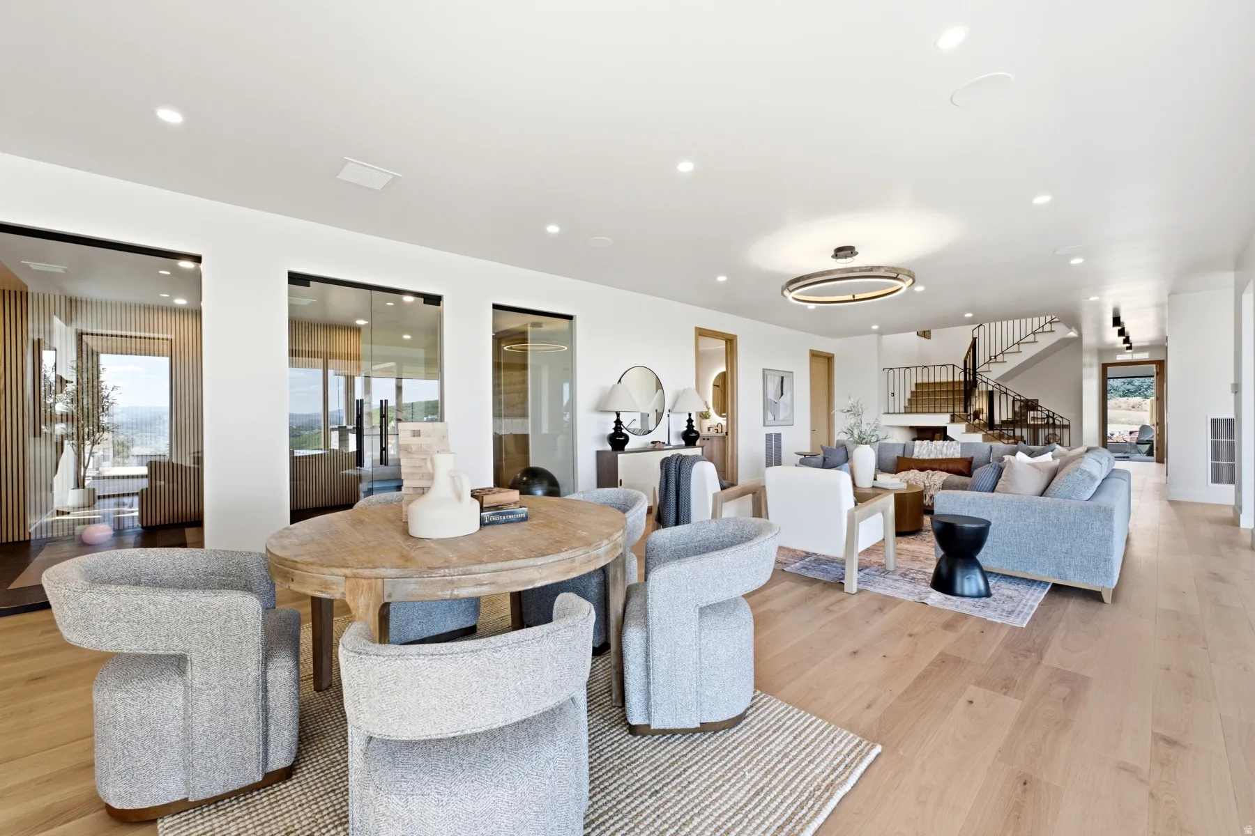 Spacious open-concept living area featuring light wood-finish flooring, recessed lighting, and a modern circular chandelier