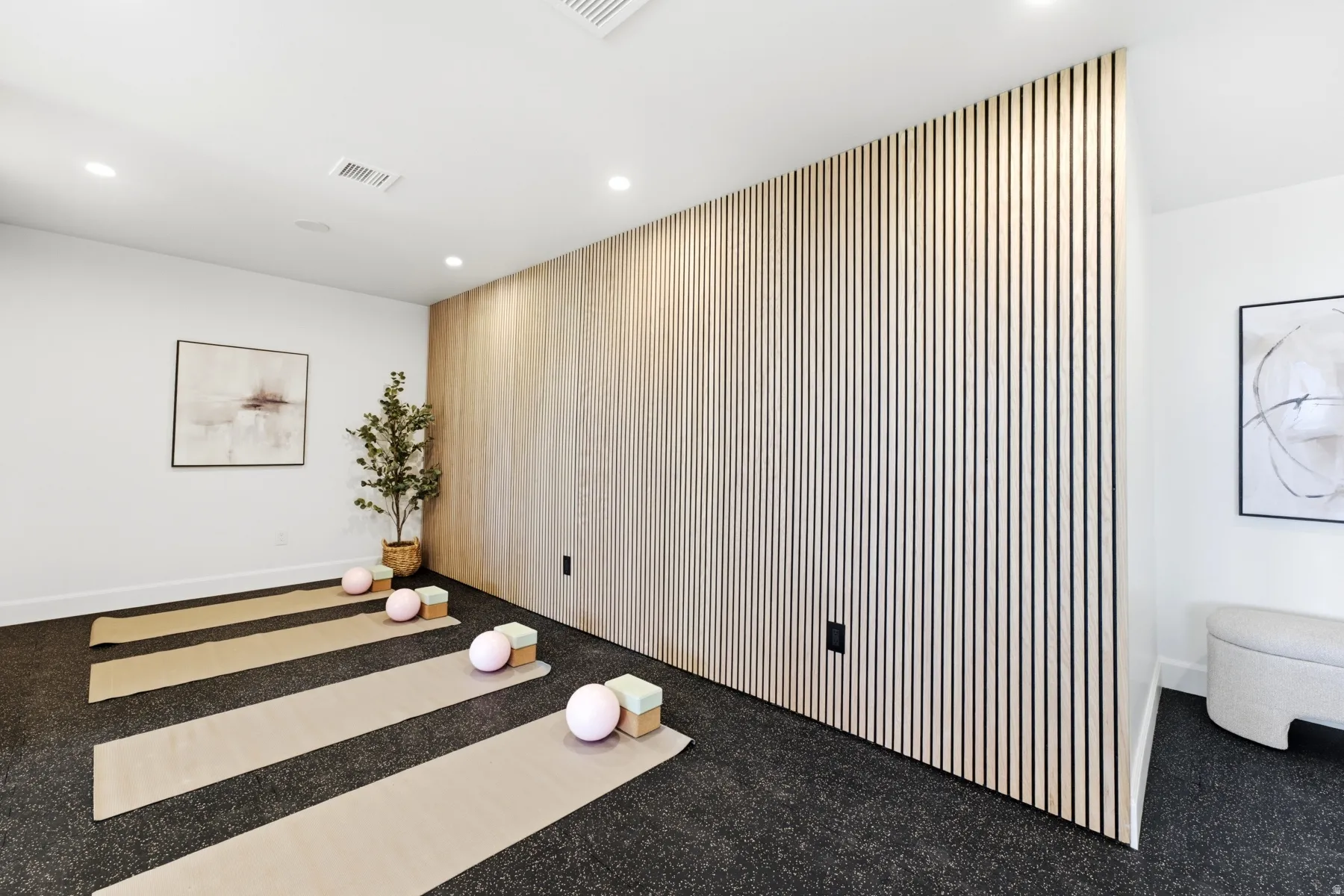 Recessed lighting illuminates a versatile room featuring a full wall with vertical slat wood-finish paneling
