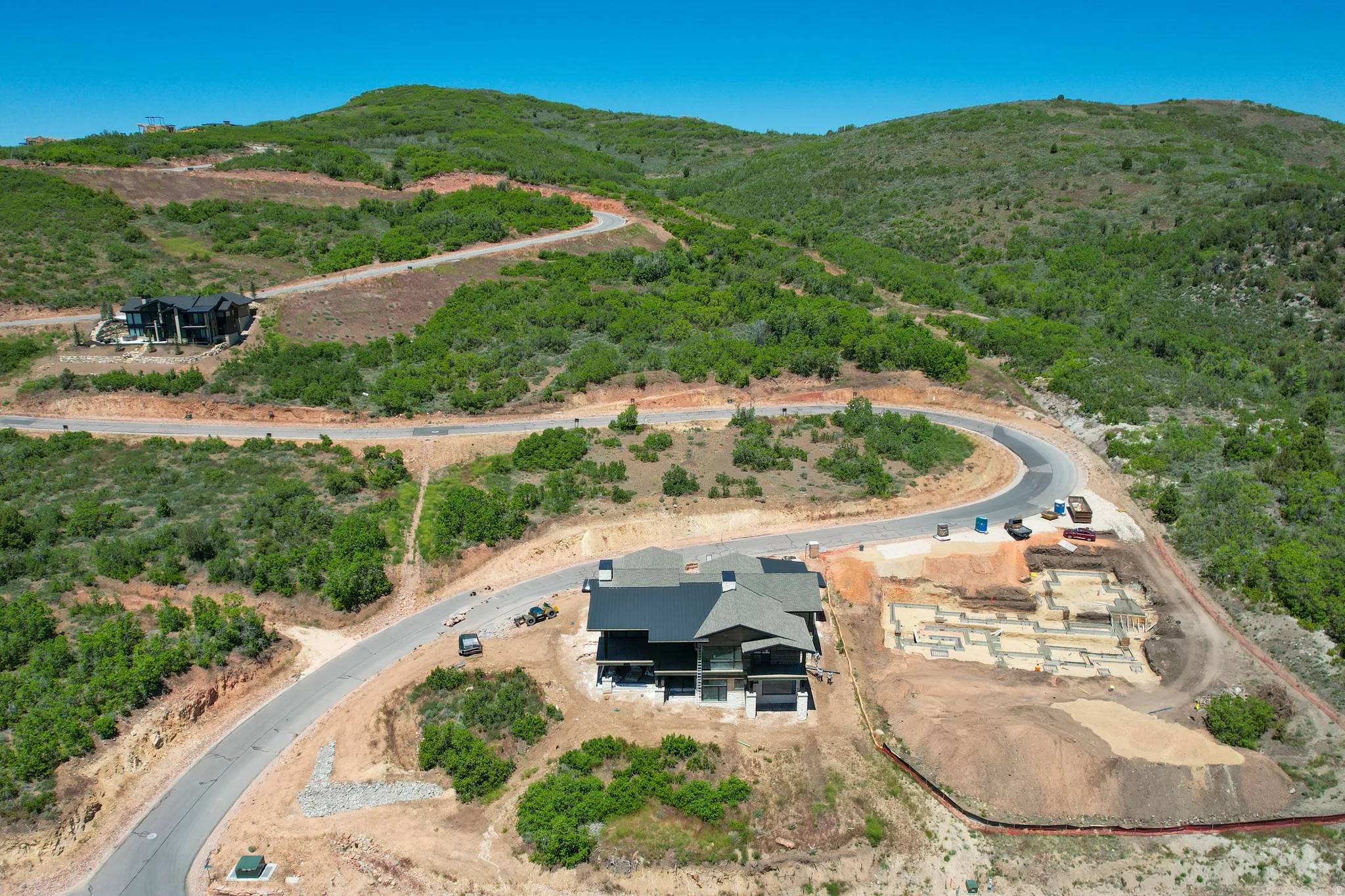 Hillside property featuring a modern architectural residence with a dark exterior, a pitched roof, and a visible foundation