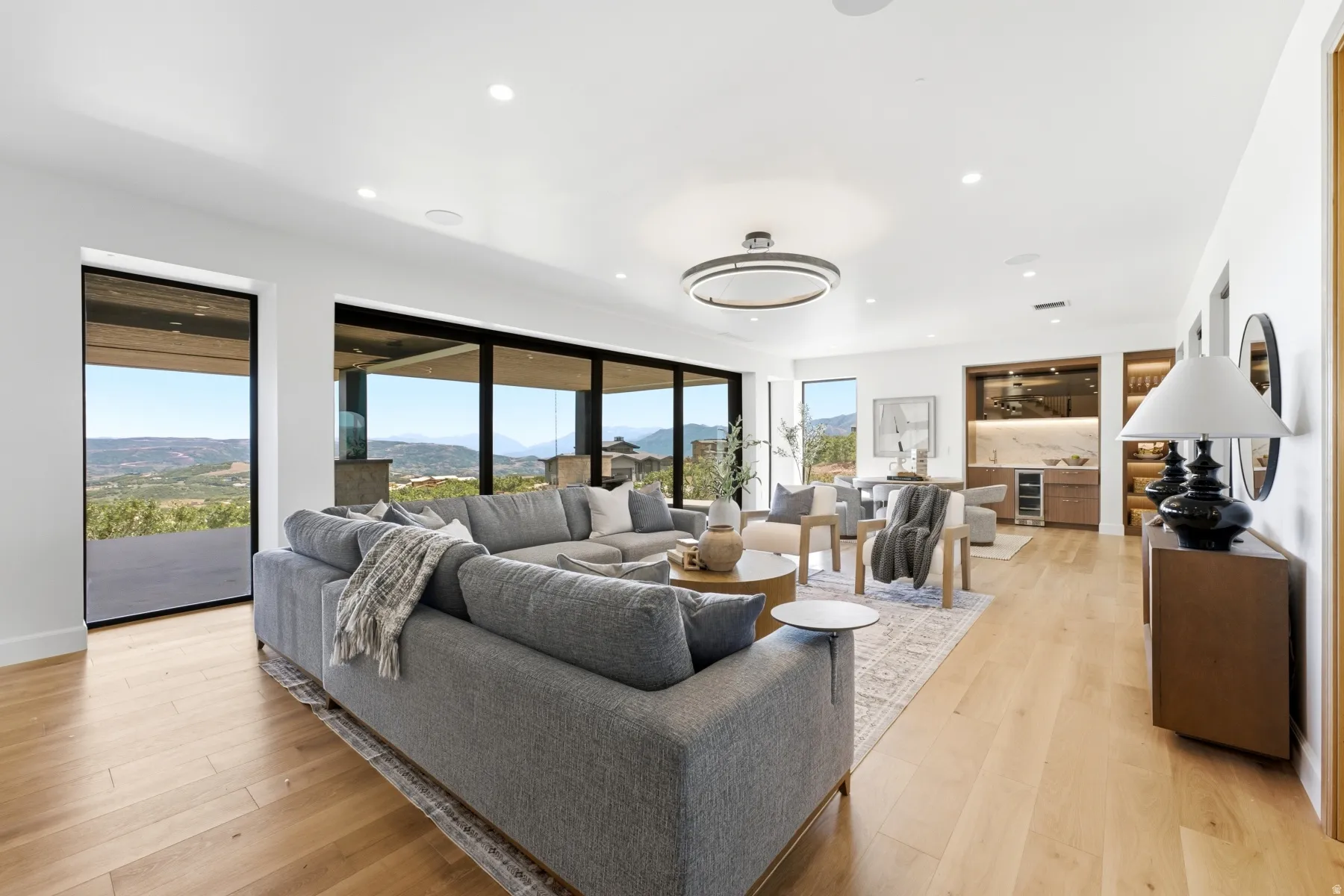 Open-concept living area featuring expansive glass sliding doors, wood-finish flooring, a built-in wet bar with a wine refrigerator, and recessed lighting