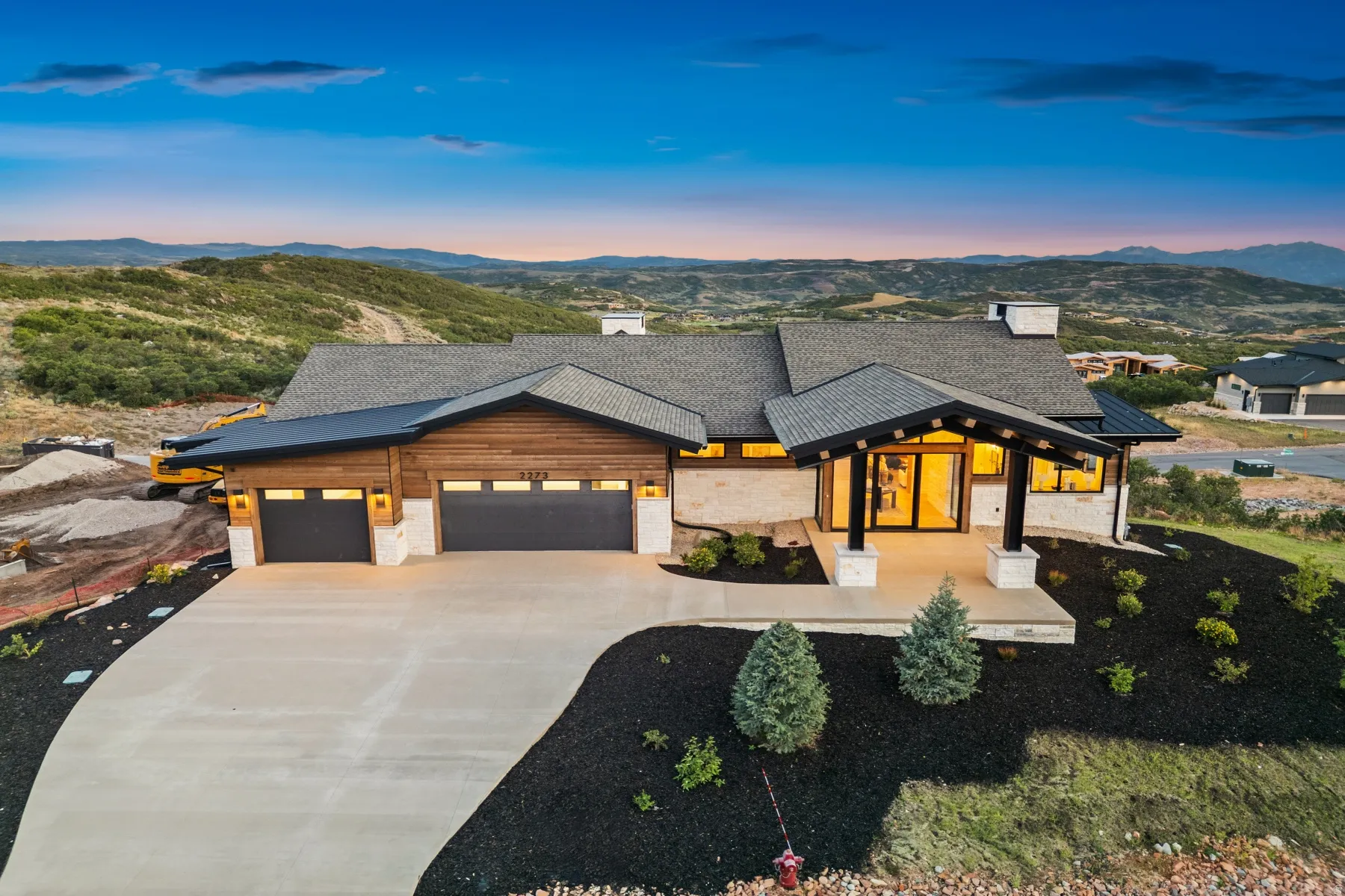 Modern architectural design featuring prominent gables, stone and wood-panel siding, and a multi-car garage with dark doors