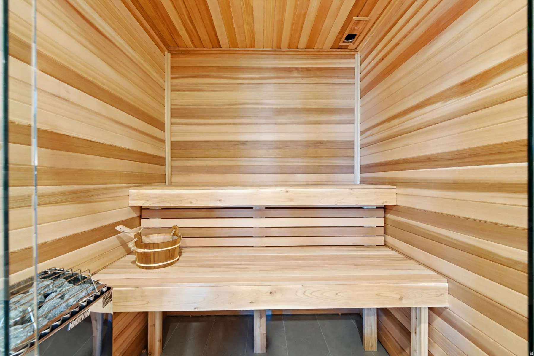 Cedar-paneled sauna featuring a built-in bench, glass enclosure, and stone heater