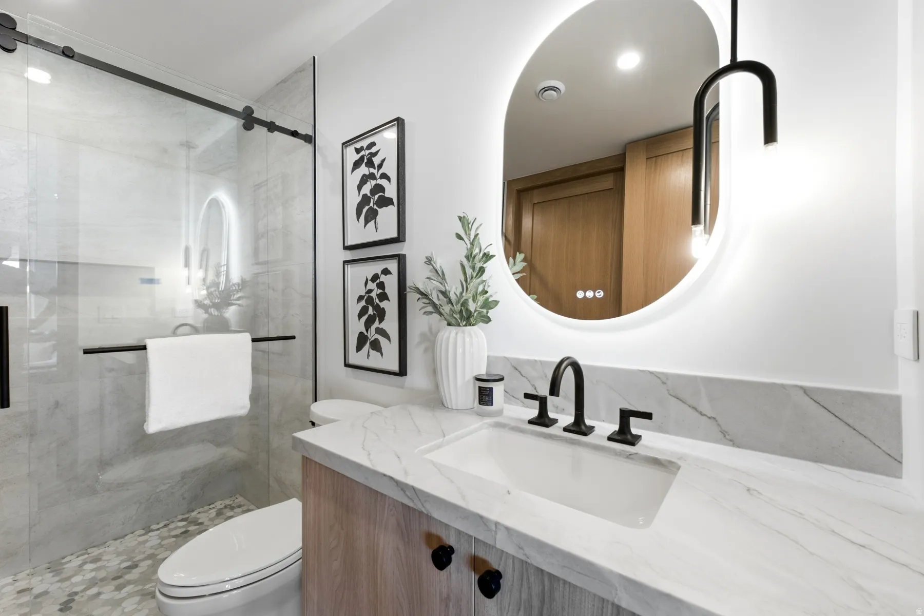 Bathroom featuring a walk-in shower with glass enclosure, a vanity with a white countertop and integrated sink, a back-lit oval mirror, and a wood-finish vanity cabinet