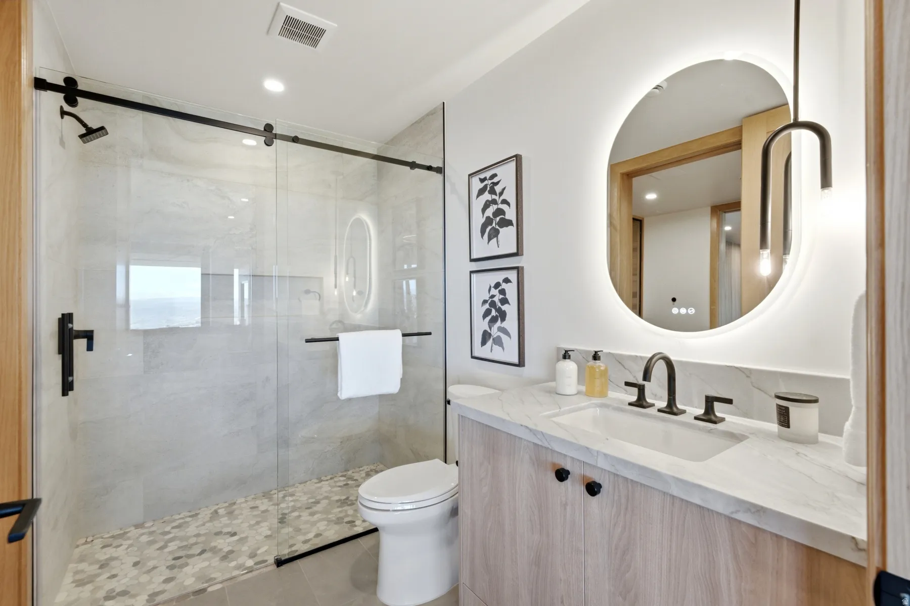 Glass-enclosed shower with pebble-tile flooring and matte black fixtures