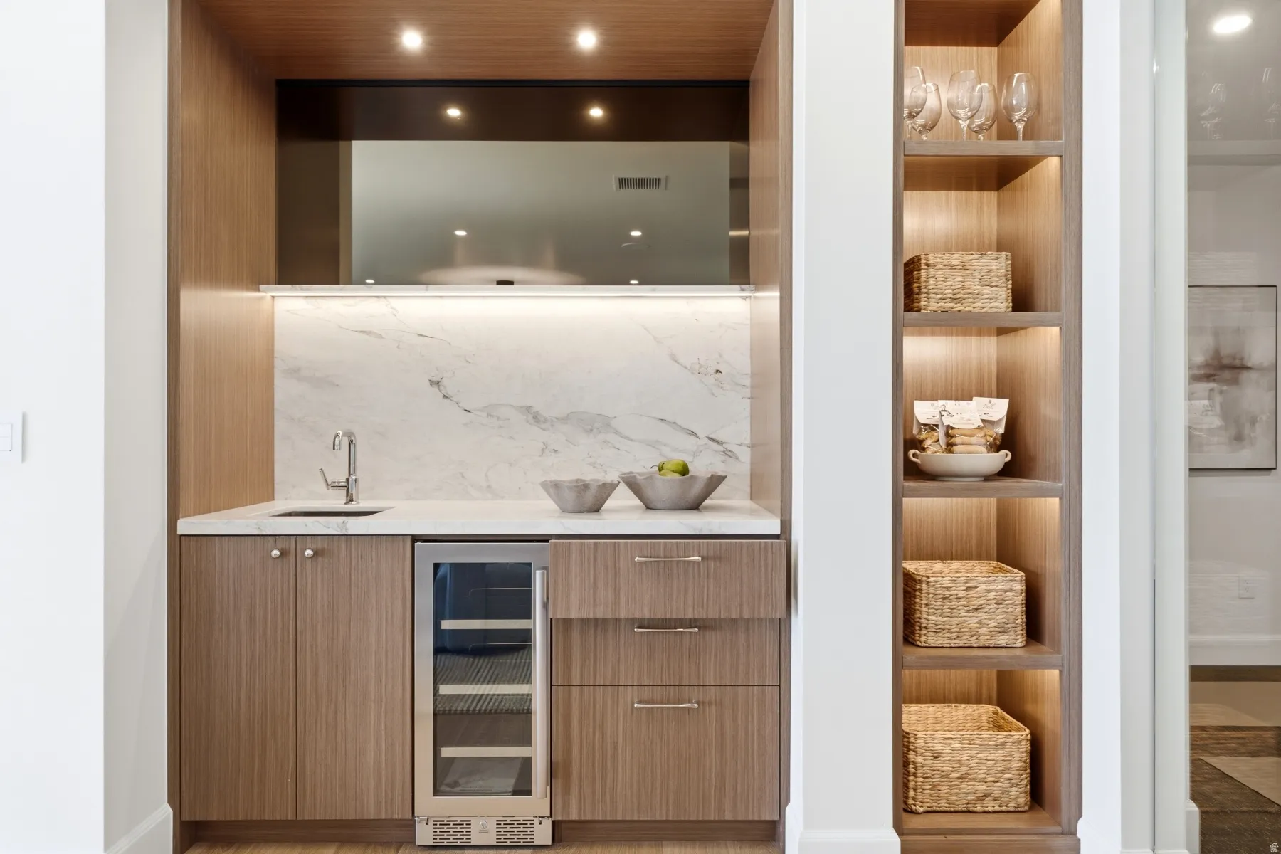 Built-in wet bar featuring a beverage cooler, integrated sink with faucet, white countertop, and marble-patterned backsplash
