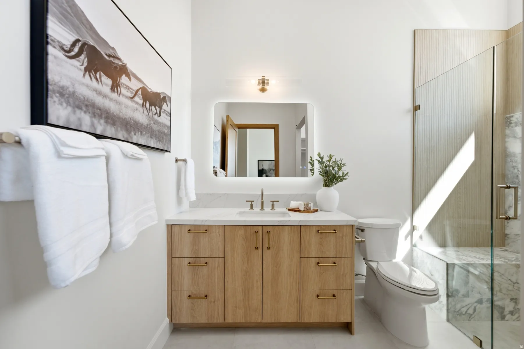 Light wood-finish vanity with a light countertop, rectangular under-mount sink, and framed mirror with integrated lighting