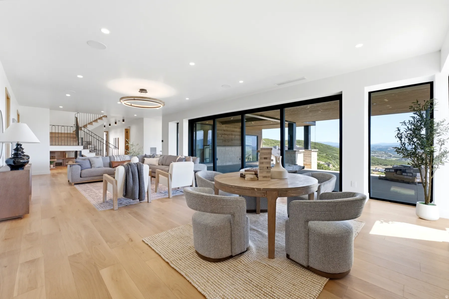 Expansive living area featuring light wood-finish flooring, recessed lighting, a modern chandelier, and large sliding glass doors opening to an outdoor area