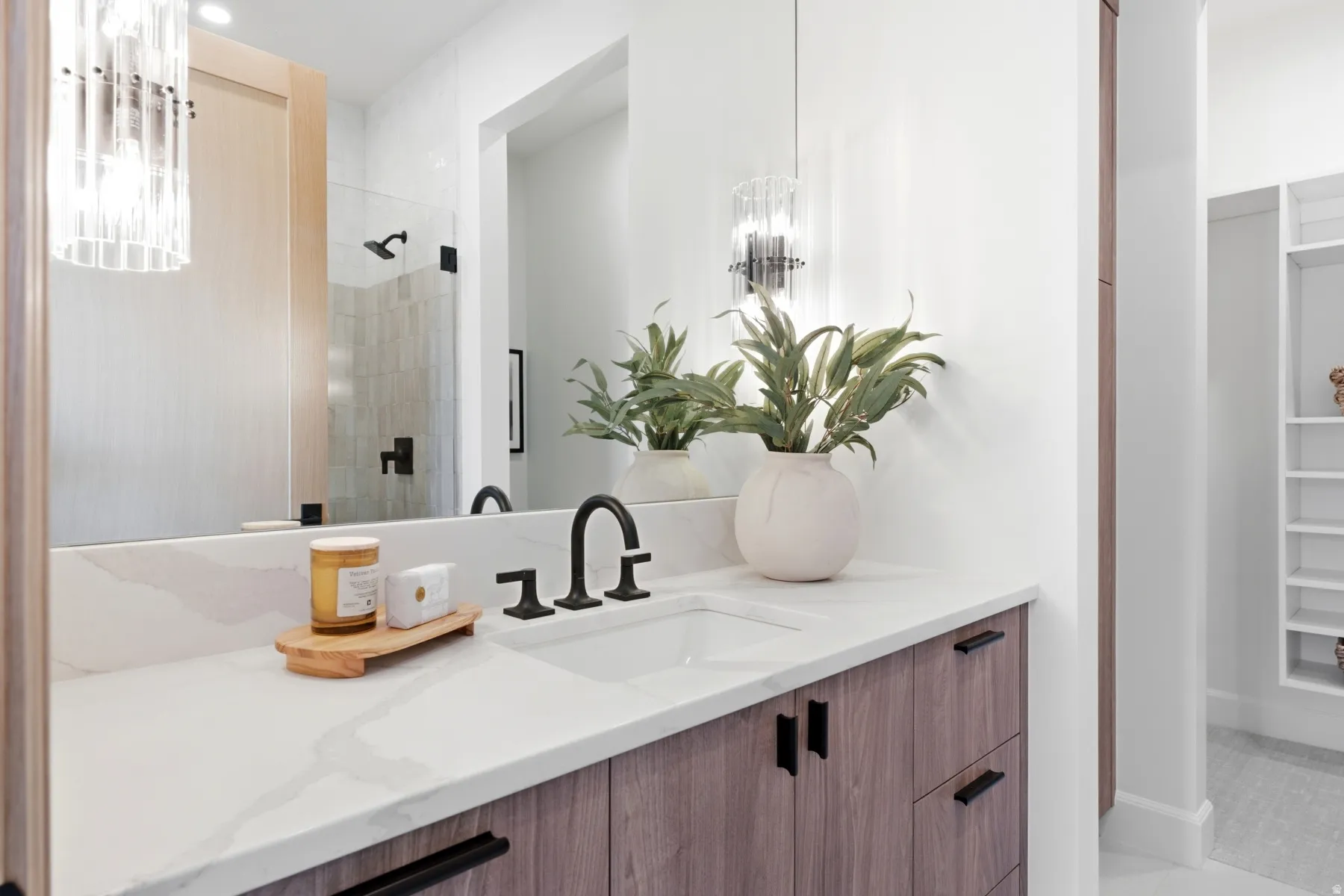 Bathroom vanity featuring a light-toned wood-finish cabinetry, quartz-style countertop, and matte black fixtures