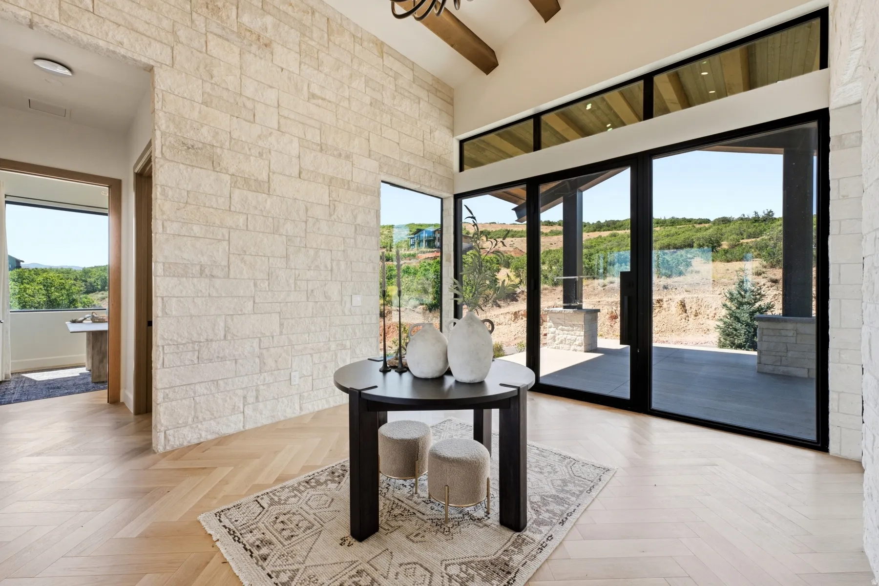 Grand entry featuring a stone accent wall, herringbone wood-finish flooring, vaulted ceiling with exposed beam, and expansive glass doors opening to a covered patio