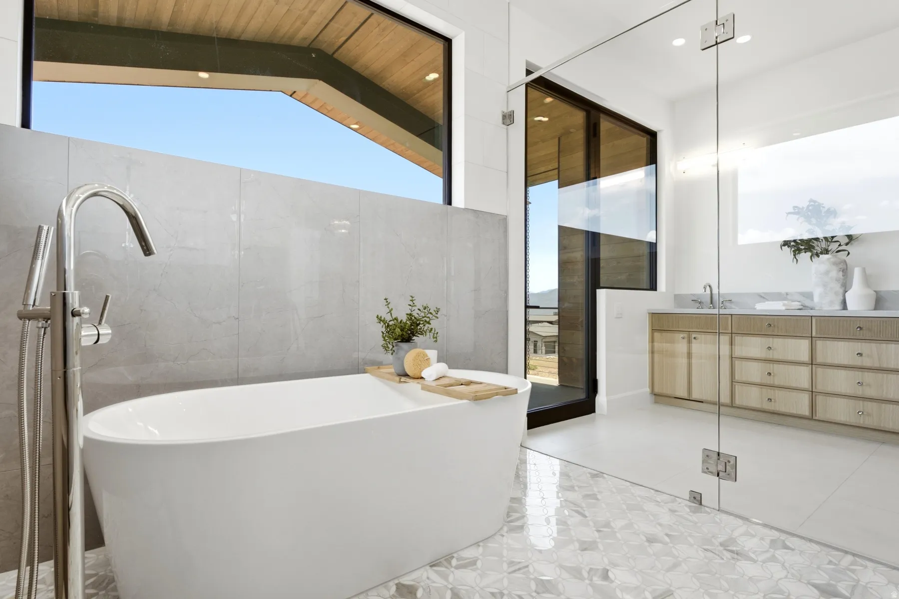 Freestanding soaking tub with a floor-mounted polished chrome faucet, set against a tiled accent wall and large picture window
