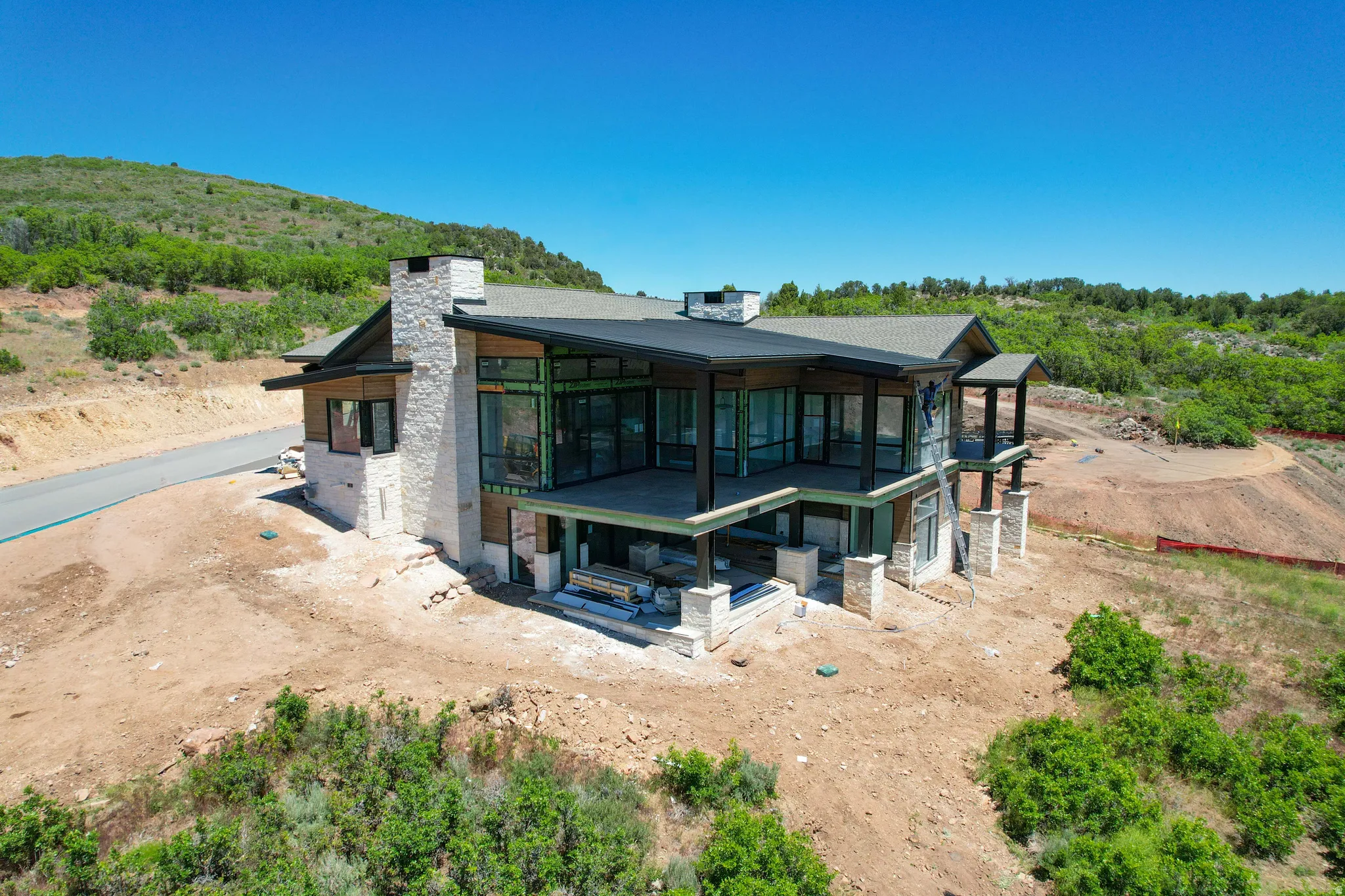 Contemporary architectural design featuring extensive window walls, multiple balconies, a stone-clad chimney, and a dark shingled roof
