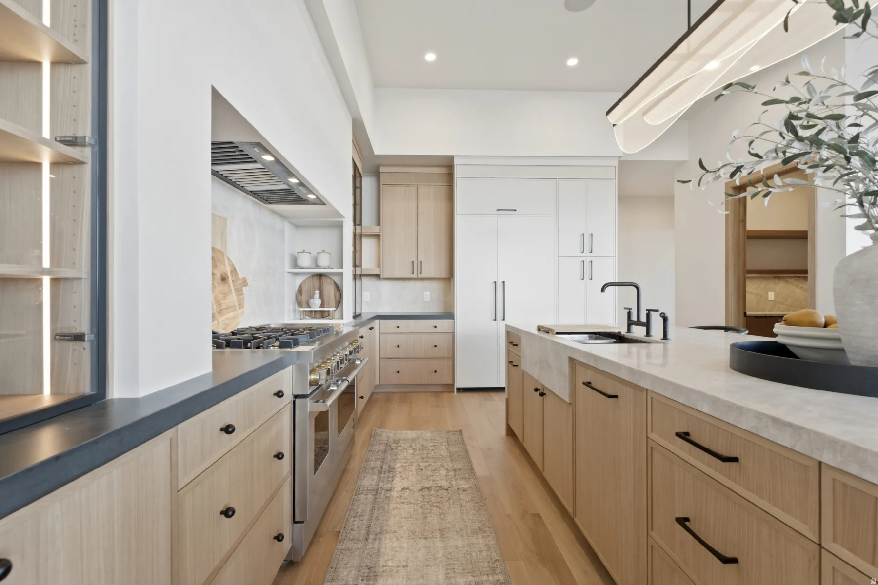 Gourmet kitchen with professional-grade stainless steel range, custom light wood-finish cabinetry, a large center island with integrated sink, stone countertops, and recessed lighting