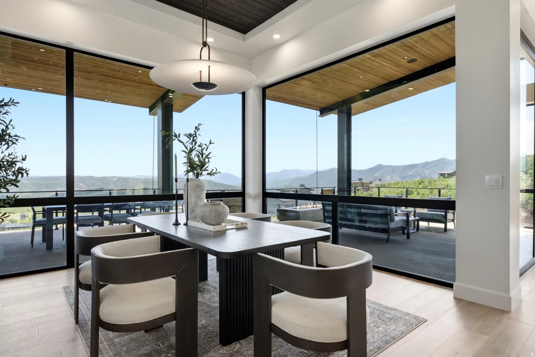 Open-concept dining area featuring expansive floor-to-ceiling windows, light wood-finish flooring, and direct access to an outdoor patio with mountain scenery