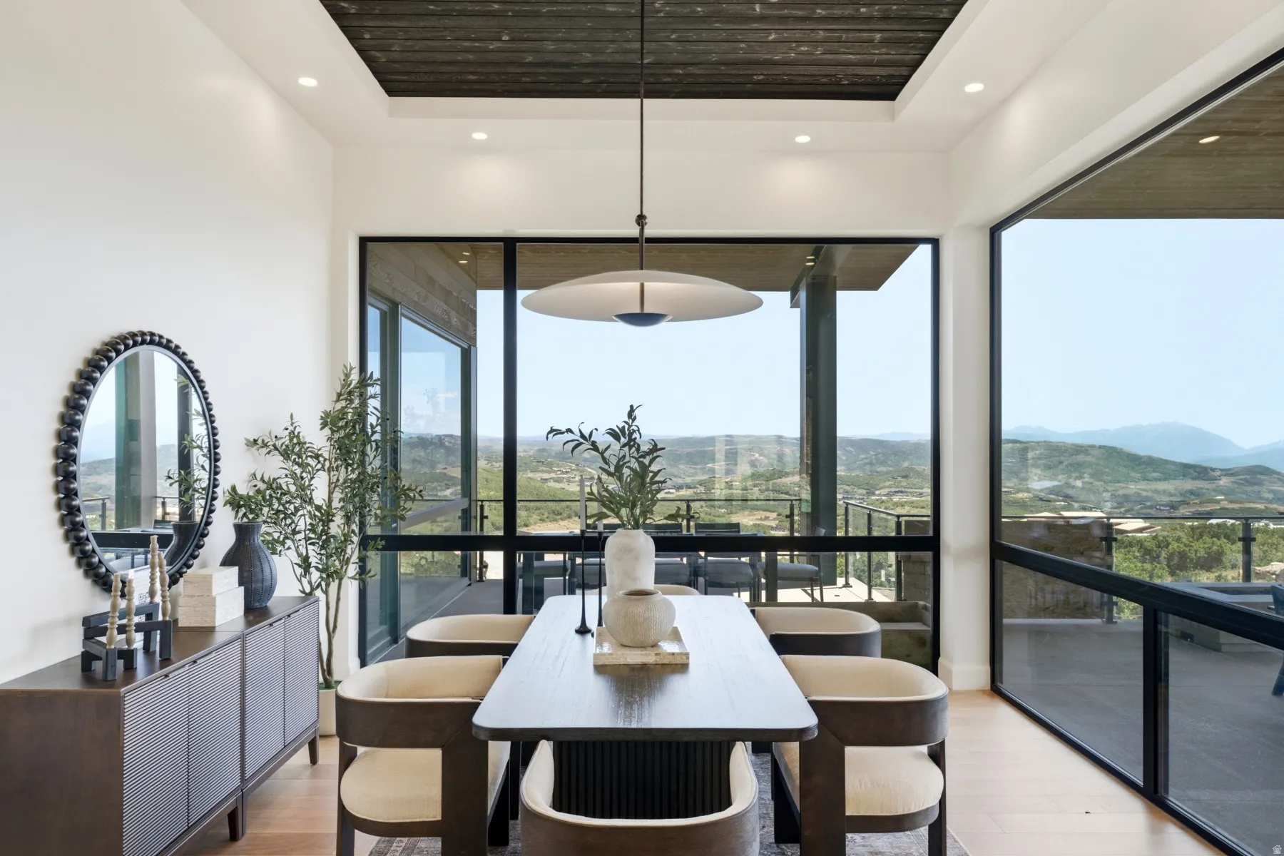 Open-concept dining area featuring expansive floor-to-ceiling windows, light wood-finish flooring, and a recessed ceiling with wood paneling
