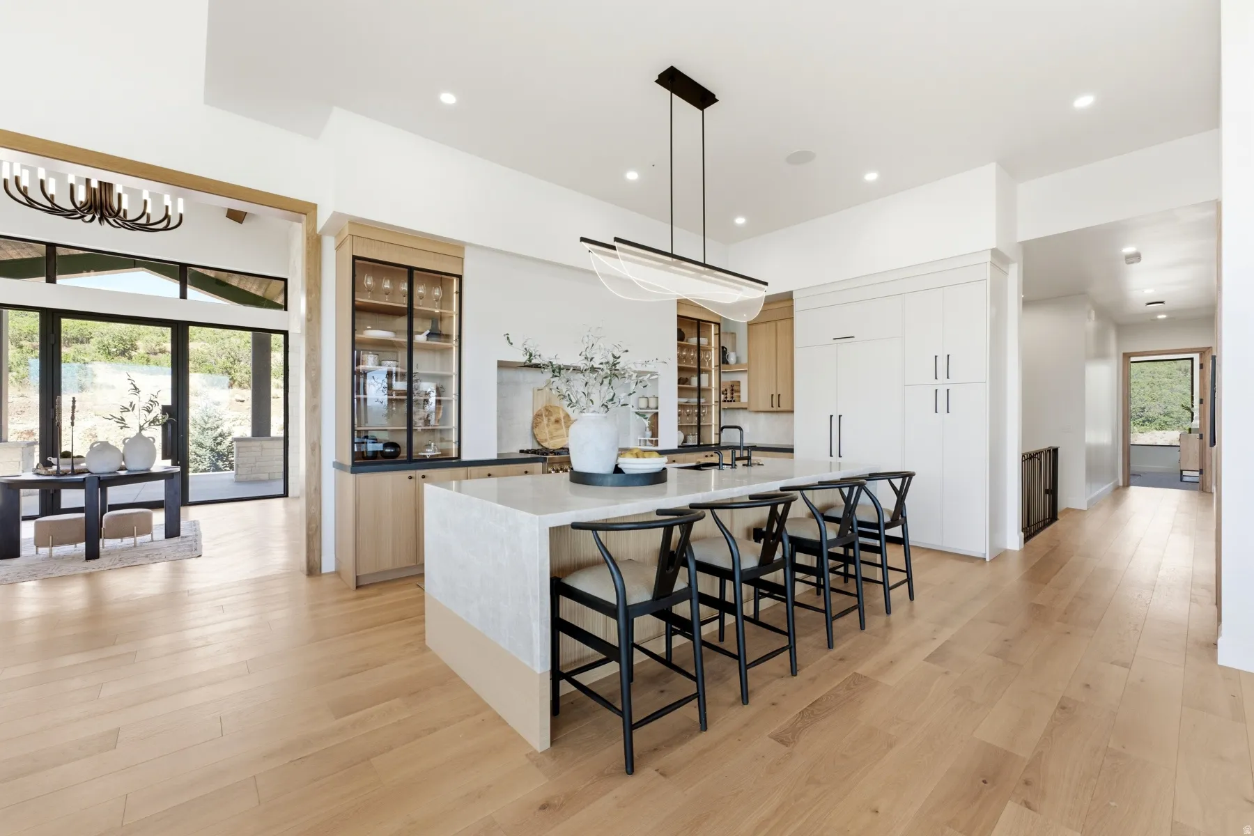 Open-concept kitchen featuring an expansive island with seating, wood-finish flooring, built-in display cabinetry, and a modern linear chandelier