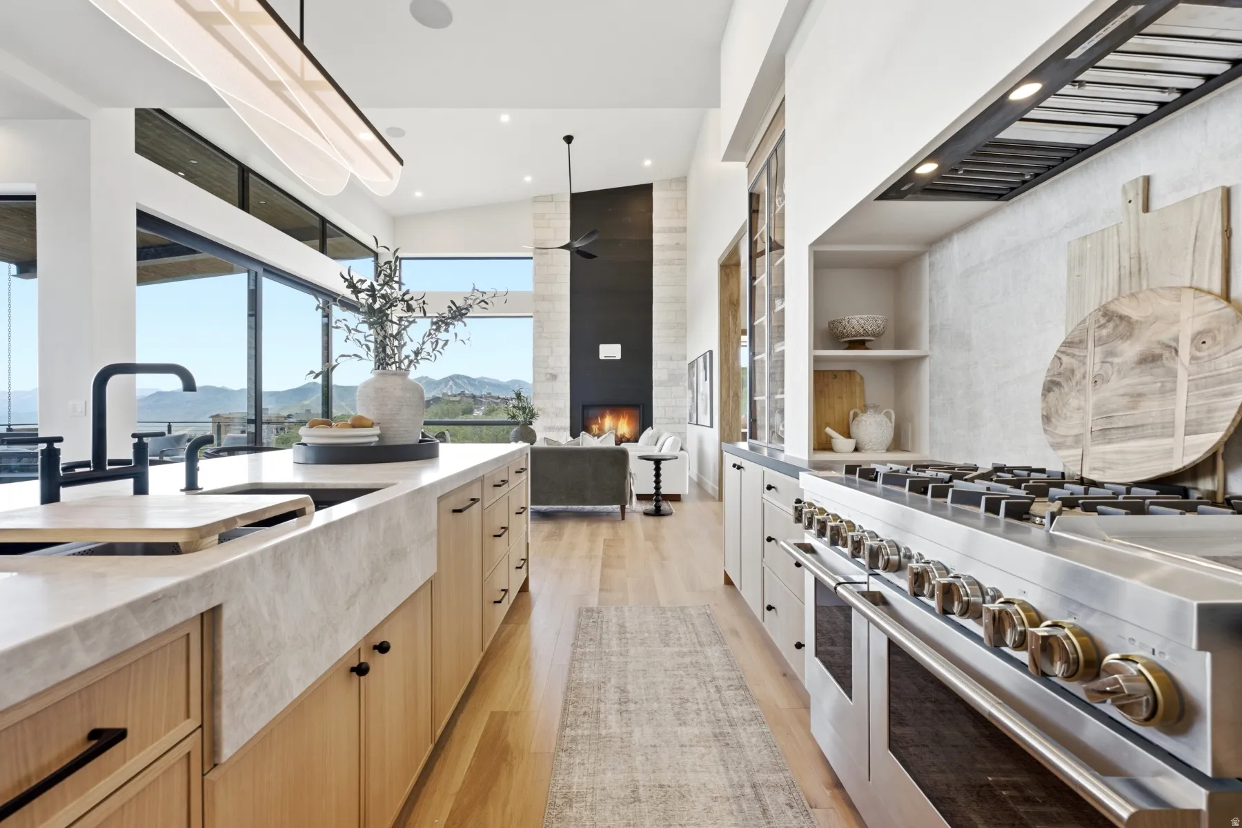 Gourmet kitchen with a large stone island featuring a farmhouse sink and modern black faucet, professional-grade stainless steel range with overhead ventilation, light wood-finish flooring, and expansive sliding glass doors