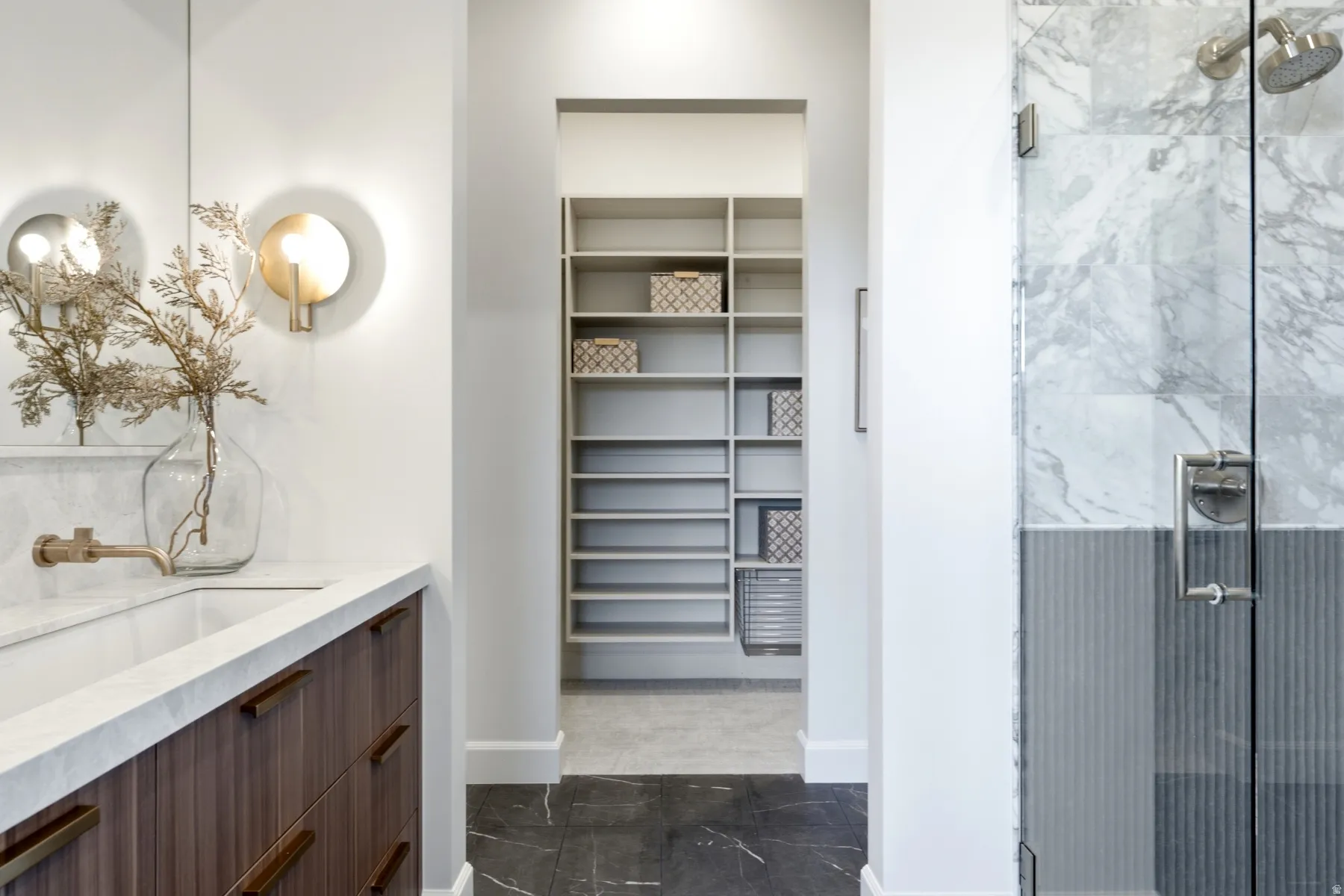 Bathroom featuring a wood-finish vanity with an integrated sink and wall-mounted faucet, complemented by a glass-enclosed shower with full-height marble-look tile