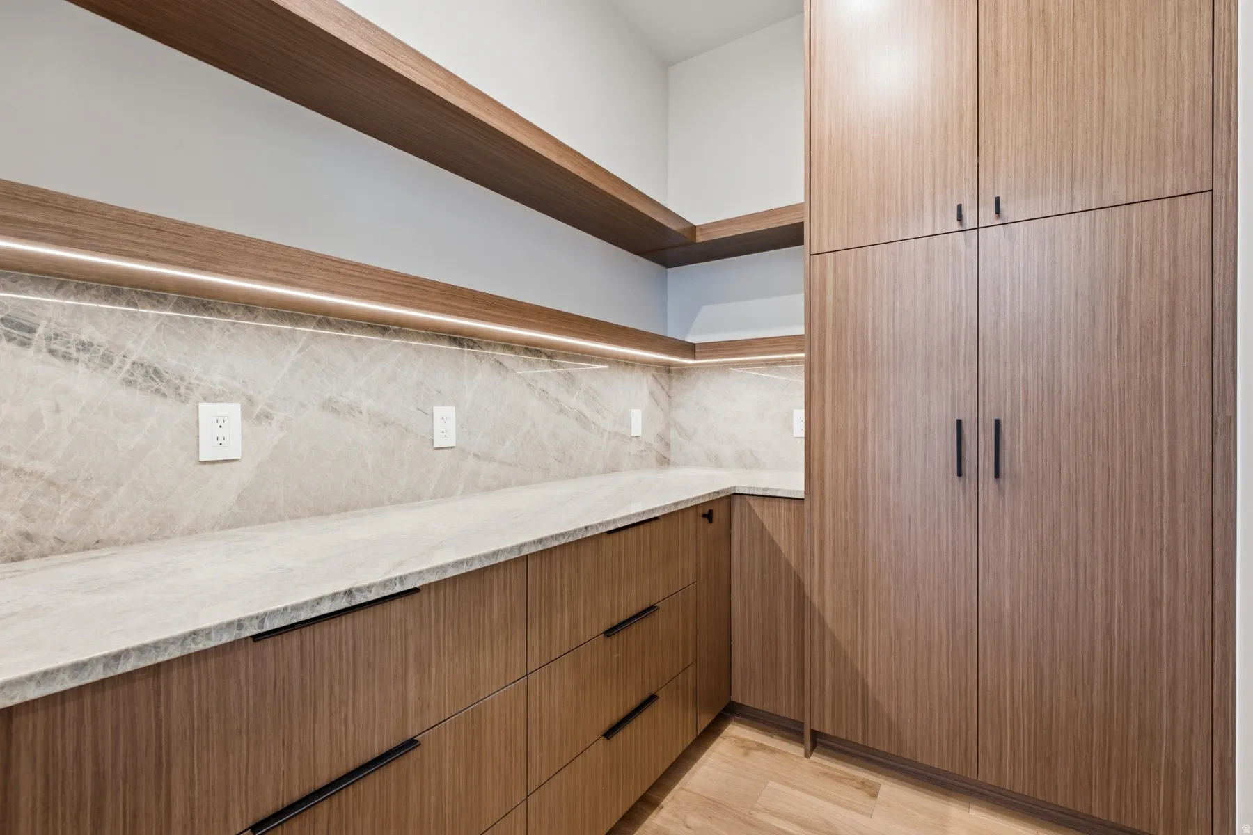 Custom wood-finish cabinetry with black hardware, under-cabinet lighting, natural stone countertops, and a full-height stone backsplash