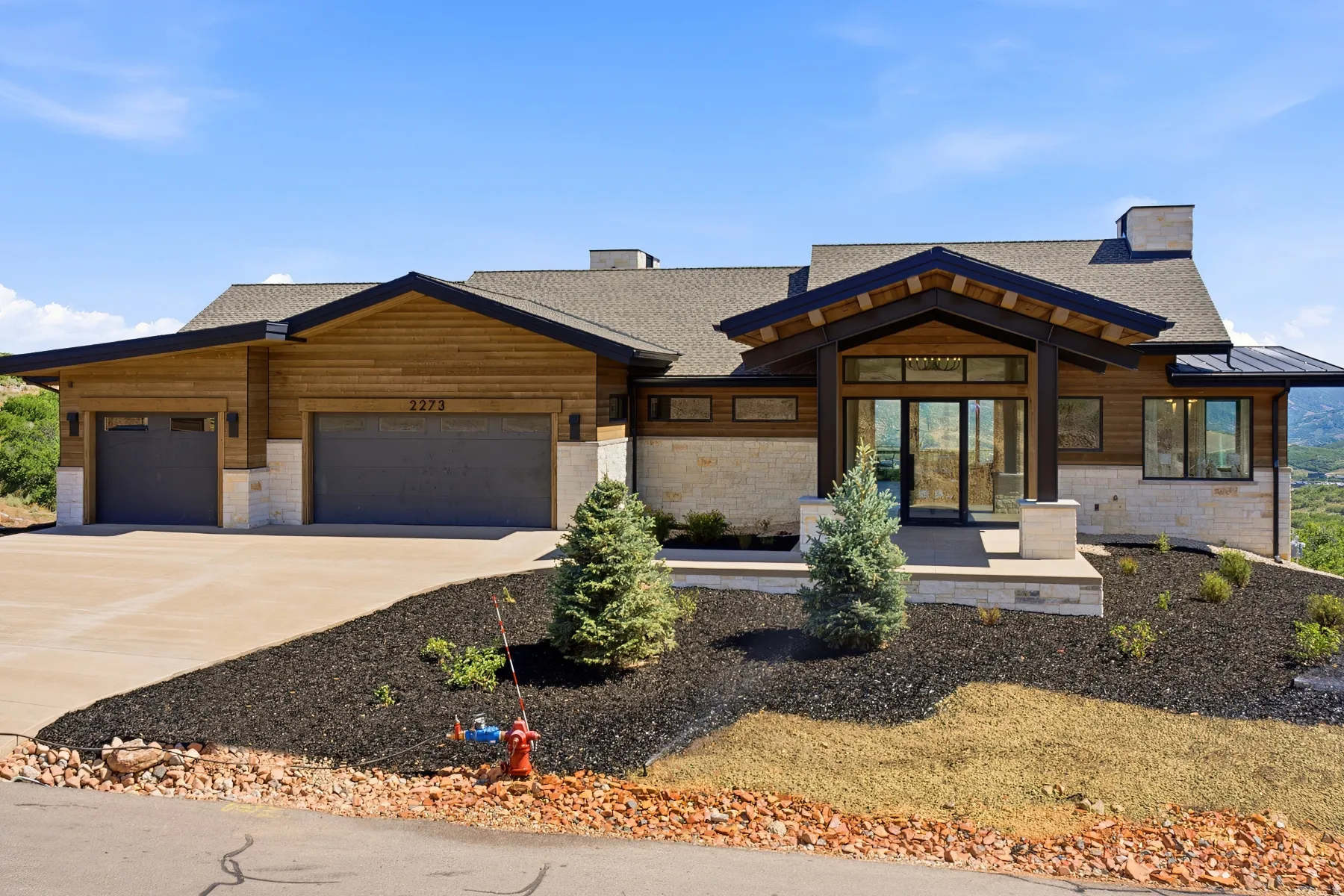 Contemporary exterior showcasing natural wood siding, stone accents, a deep-set covered entry, expansive glass doors, and a multi-car garage
