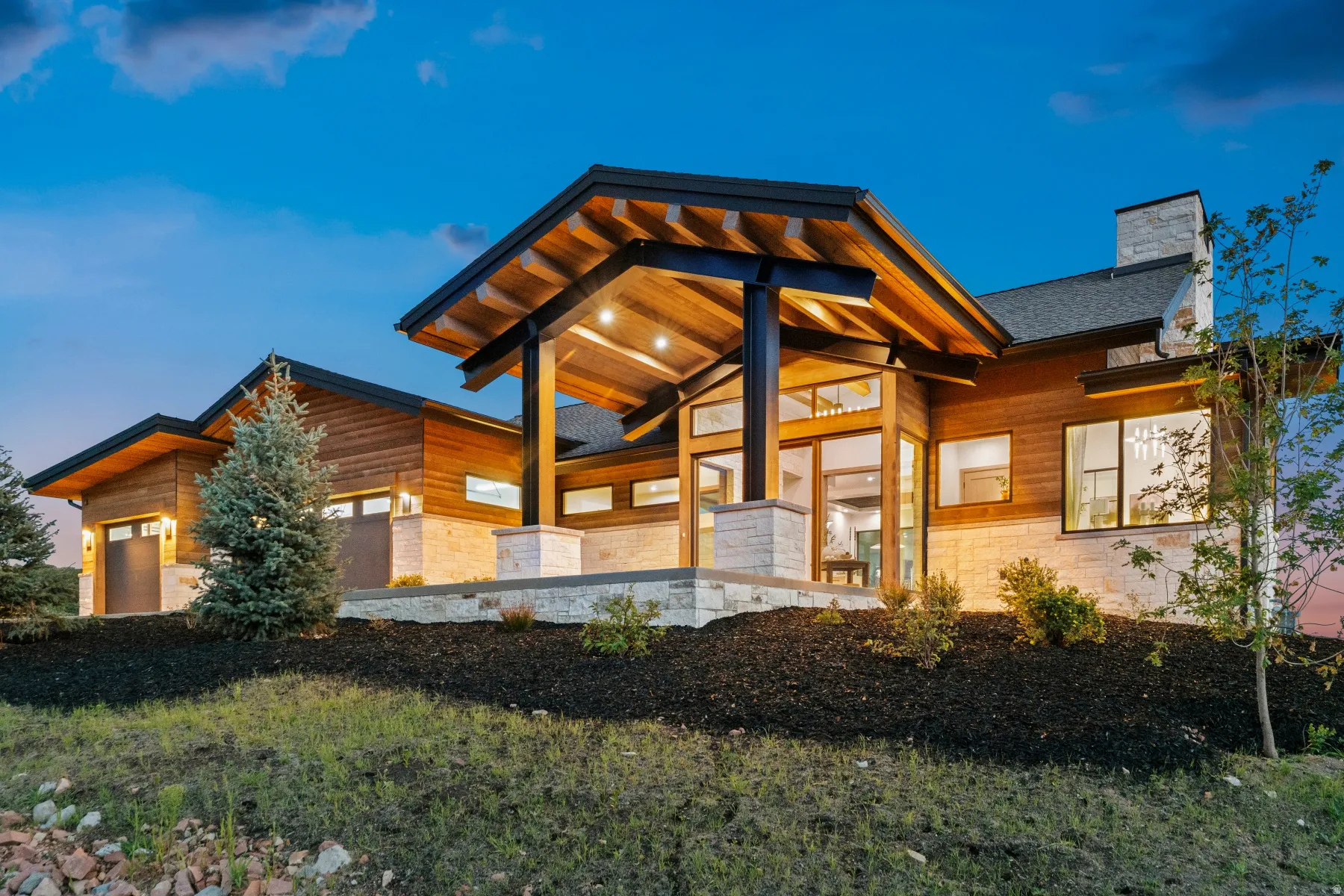 Modern exterior featuring wood siding, stone cladding, a prominent covered entry with exposed wood beams, and multiple large windows