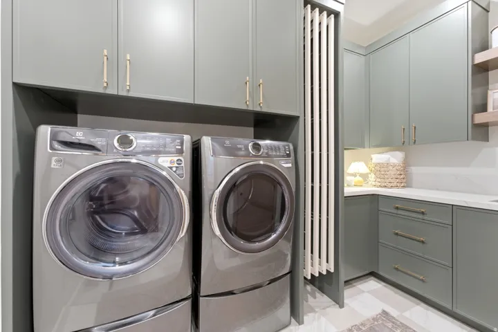 Laundry area featuring sleek grey cabinetry with gold-toned hardware, a built-in folding rack, and a white countertop