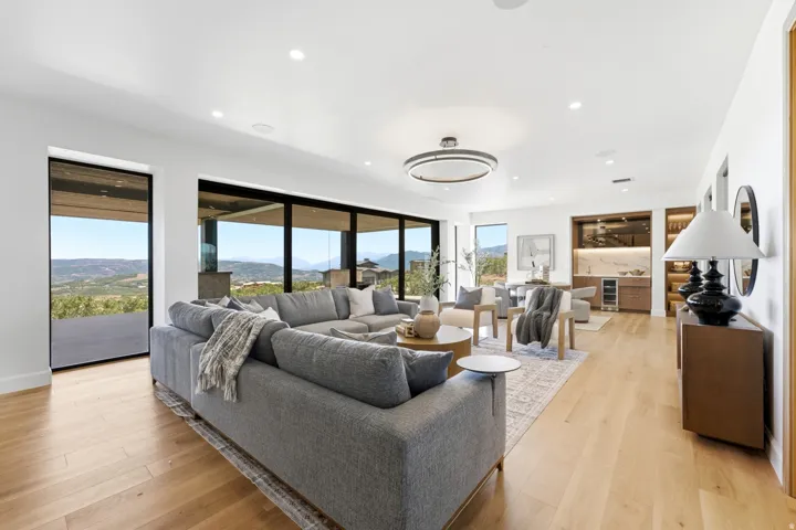 Open-concept living area featuring expansive glass sliding doors, wood-finish flooring, a built-in wet bar with a wine refrigerator, and recessed lighting