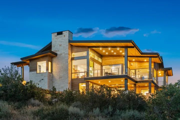 Modern architectural design featuring extensive wood paneling, a large stone chimney, and multiple balconies with glass railings