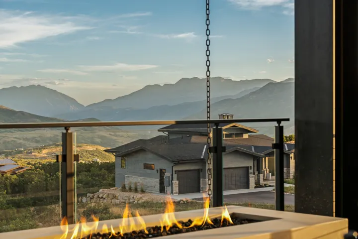 Concrete fire pit with dark fire glass, glass panel railing, and mountain scenery