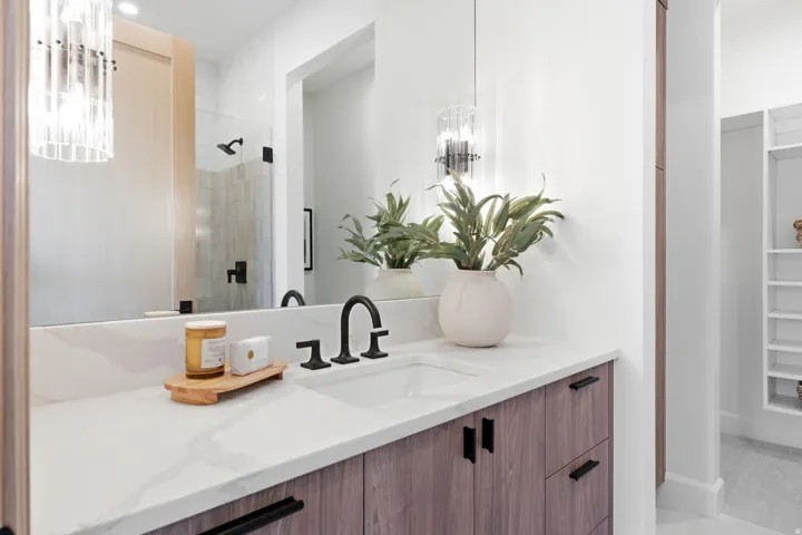 Bathroom vanity featuring a light-toned wood-finish cabinetry, quartz-style countertop, and matte black fixtures