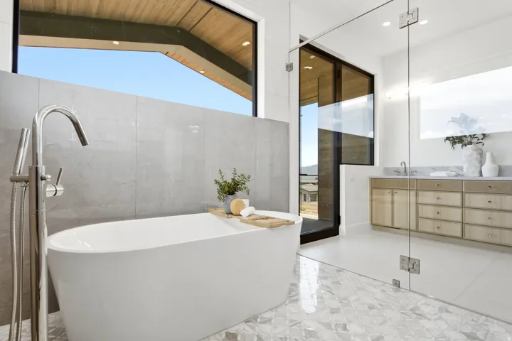 Freestanding soaking tub with a floor-mounted polished chrome faucet, set against a tiled accent wall and large picture window