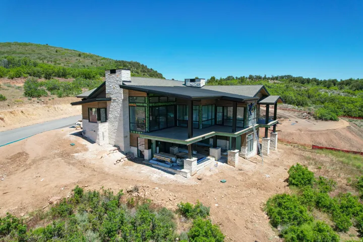 Contemporary architectural design featuring extensive window walls, multiple balconies, a stone-clad chimney, and a dark shingled roof