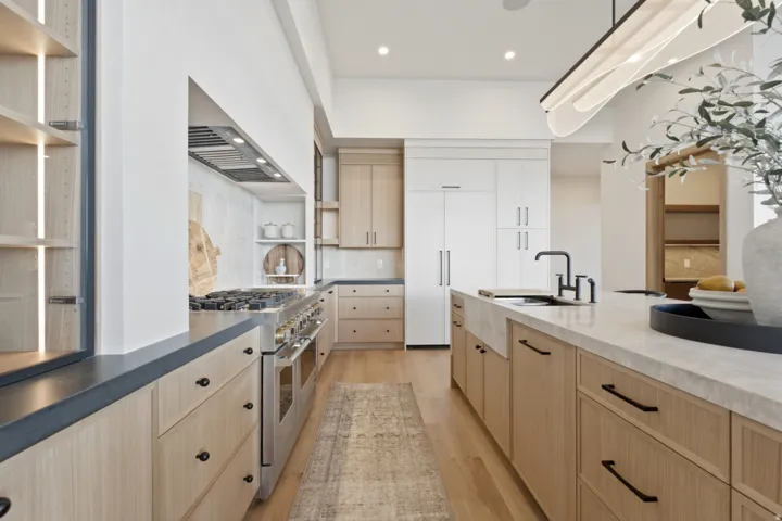 Gourmet kitchen with professional-grade stainless steel range, custom light wood-finish cabinetry, a large center island with integrated sink, stone countertops, and recessed lighting
