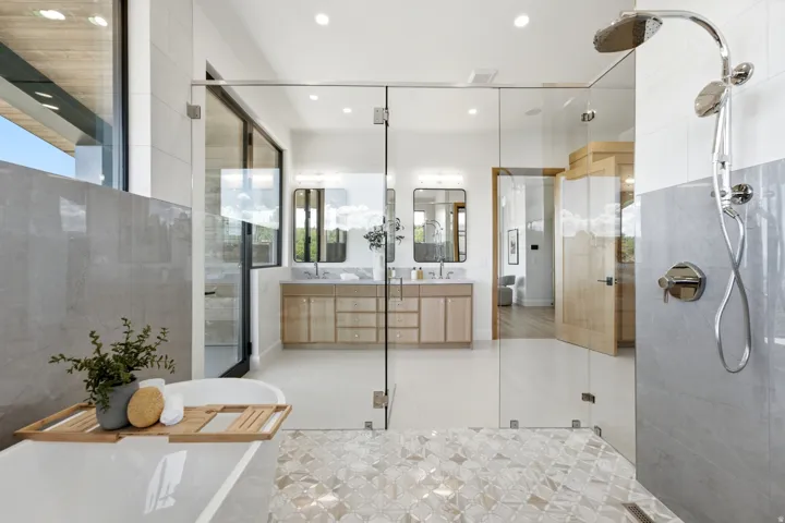 Glass-enclosed shower with multiple showerheads, dual floating vanities with undermount sinks, and a freestanding soaking tub
