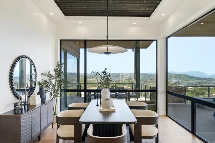 Open-concept dining area featuring expansive floor-to-ceiling windows, light wood-finish flooring, and a recessed ceiling with wood paneling