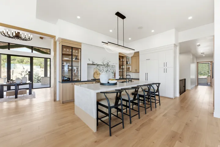 Open-concept kitchen featuring an expansive island with seating, wood-finish flooring, built-in display cabinetry, and a modern linear chandelier