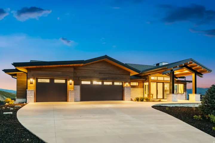 Contemporary exterior featuring wood siding, stone accents, multiple garage doors with windows, a covered entry, and a concrete driveway