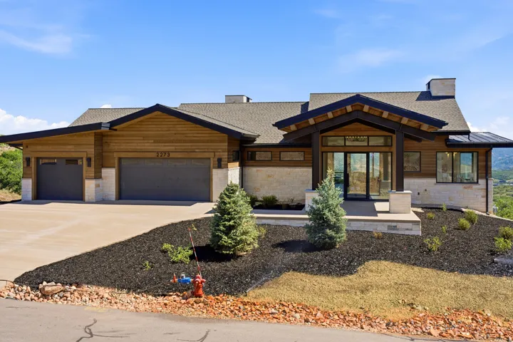 Contemporary exterior showcasing natural wood siding, stone accents, a deep-set covered entry, expansive glass doors, and a multi-car garage