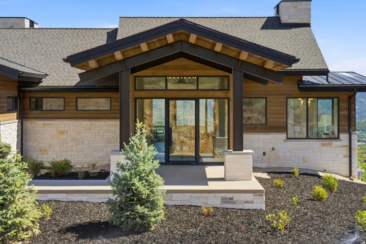 Contemporary facade featuring a stone and wood-finish exterior, covered entry with exposed beams, glass double-door entry, and a paved walkway